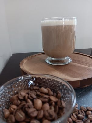 glass of latte next to a glass of coffee beans